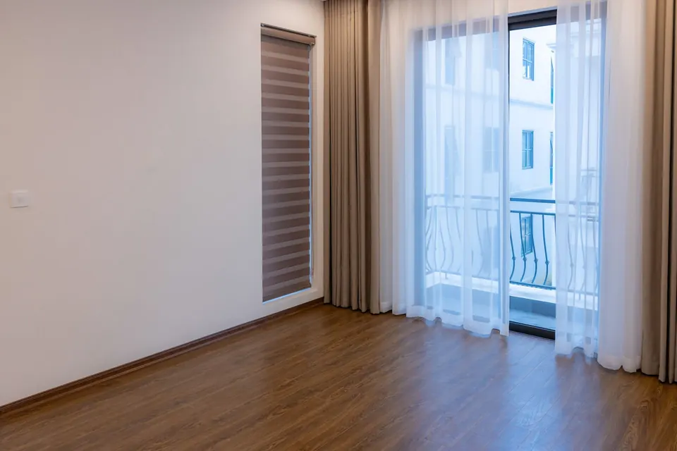 Sala com persiana rolô e cortina sobre piso de madeira